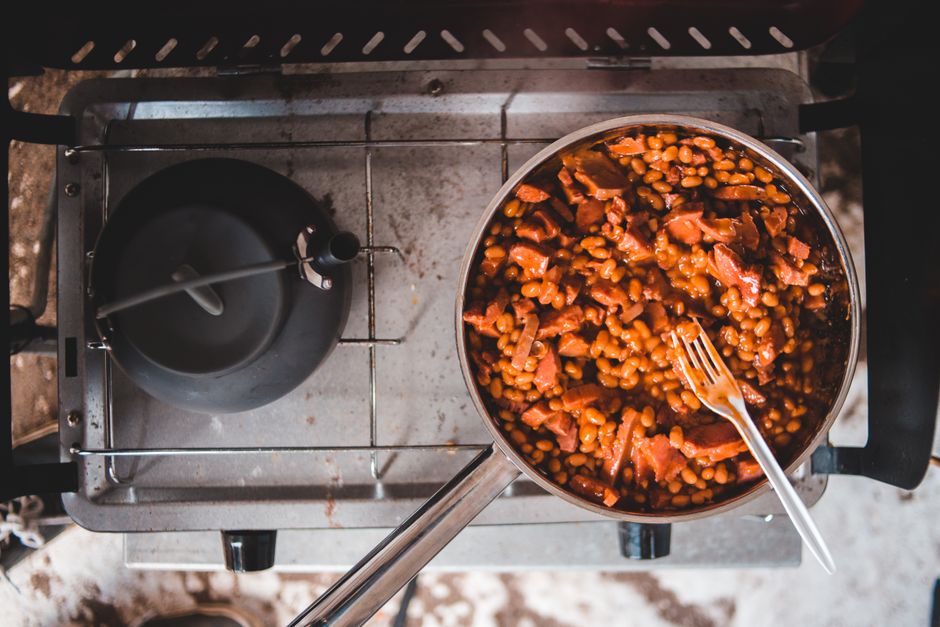 A rustic Dutch oven filled with thick, caramelized homemade baked beans studded with bacon and served with a wooden spoon resting on the side