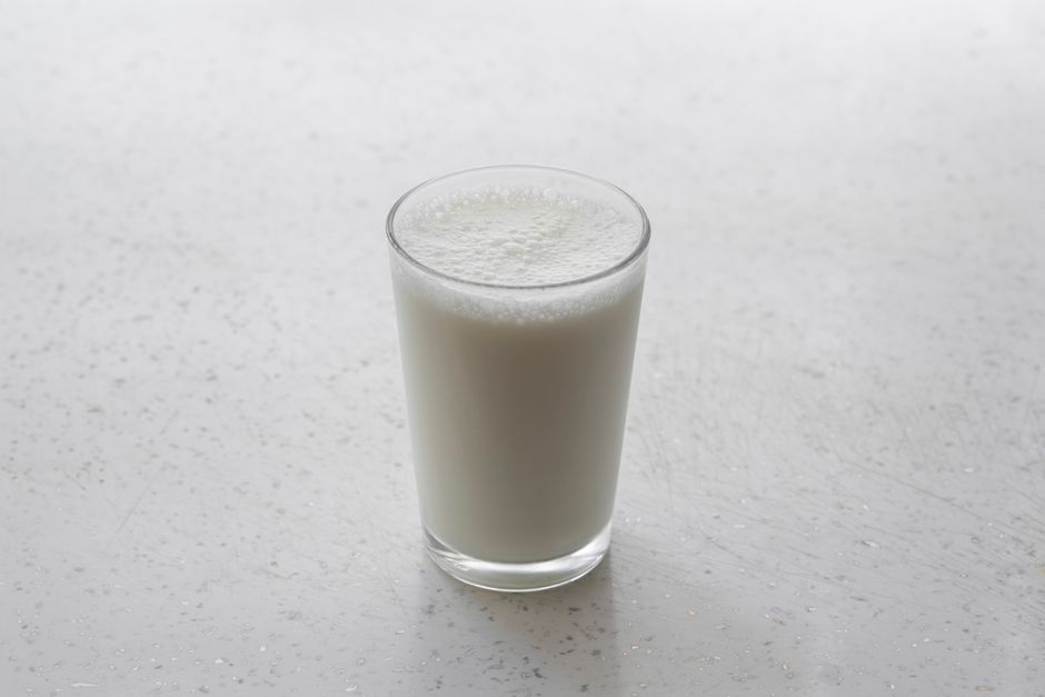 A small white saucepan of smooth, glossy bechamel sauce with a wooden spoon resting across it, shot from above on a linen dish towel