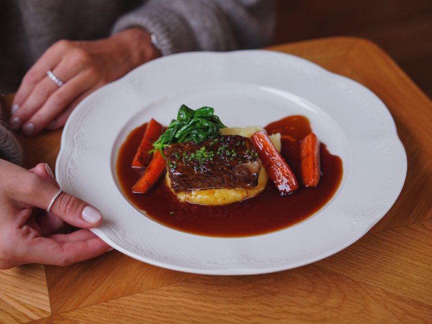 A rustic Dutch oven filled with beef bourguignon —? tender chunks of braised beef, glazed pearl onions, and mushrooms in a deep red wine sauce, garnished with fresh parsley