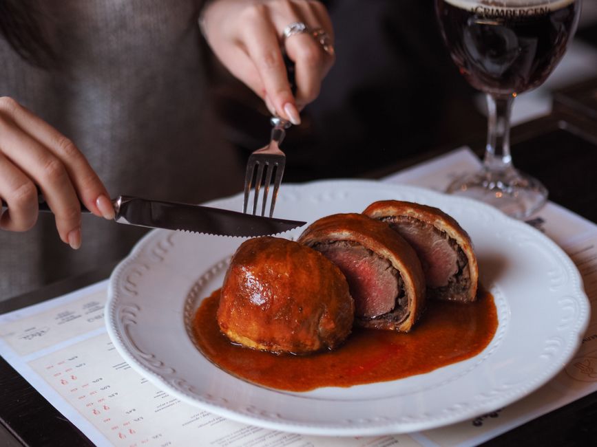 Sliced Beef Wellington on a wooden cutting board showing a perfectly medium-rare pink center surrounded by golden puff pastry and a layer of dark mushroom duxelles