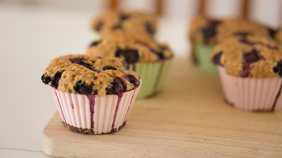 A dozen golden blueberry muffins with domed tops and a sparkling sugar crust, resting on a wire rack with fresh blueberries scattered around them