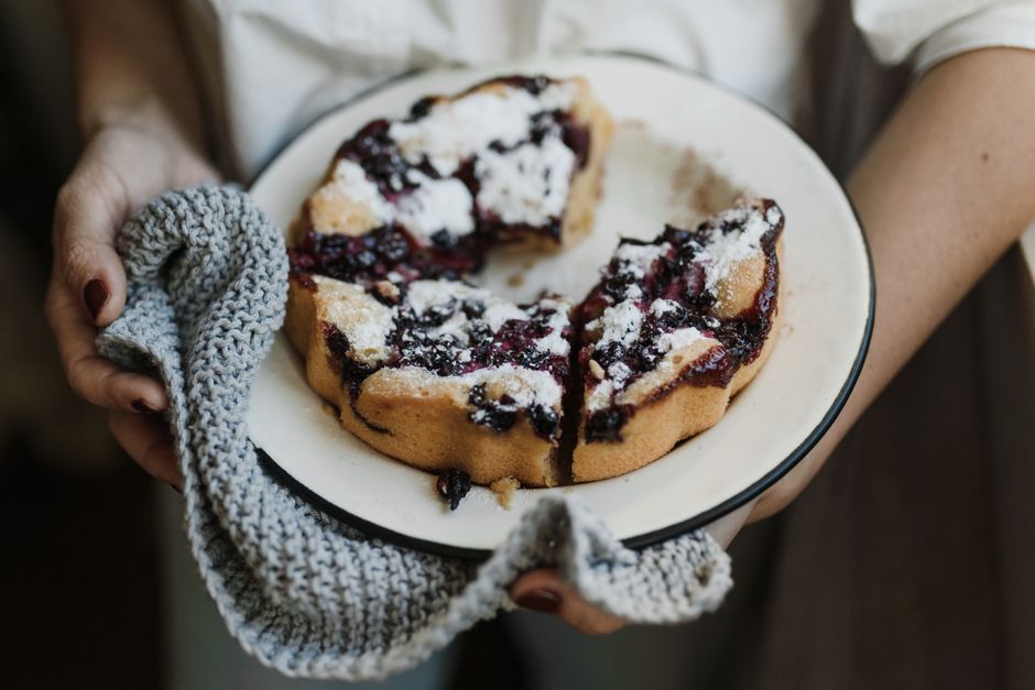 A golden-brown homemade blueberry pie with a flaky double crust and visible vent slits, resting on a wire rack with purple filling bubbling through the top