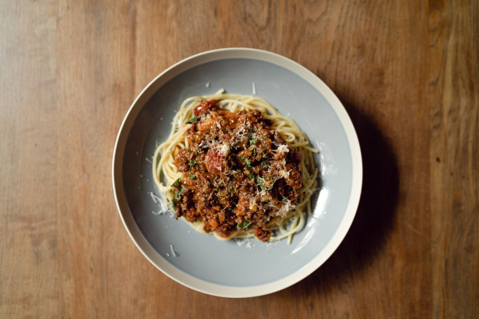 A wide bowl of tagliatelle topped with thick, glossy classic bolognese sauce, finished with freshly grated Parmesan and a crack of black pepper on a wooden table