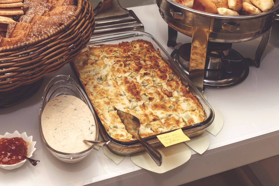 A golden-topped breakfast casserole in a white ceramic 9x13 baking dish, sliced to show layers of sausage, egg custard, melted cheddar cheese, and bread, garnished with sliced green onions
