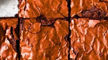 Close-up of a stack of fudgy homemade brownies with a crackly shiny top and dense chocolate interior, cut into squares on a piece of parchment paper