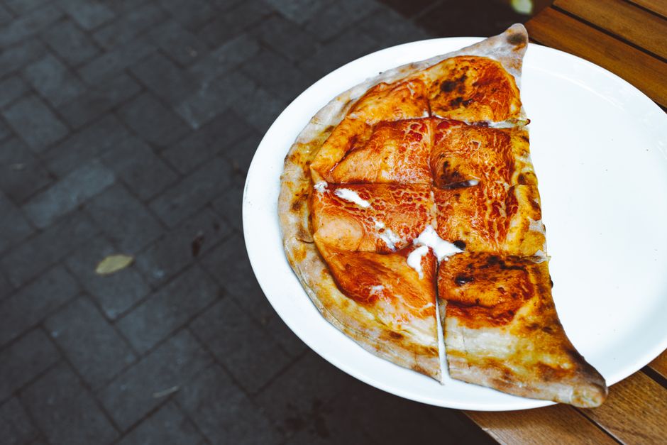 A golden-brown homemade calzone on a white plate, sliced open to reveal melted mozzarella and ricotta filling, with a small bowl of marinara sauce for dipping