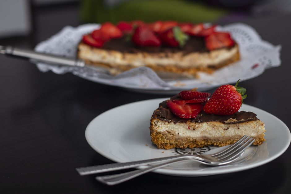 Whole classic New York-style baked cheesecake on a white cake stand with a golden graham cracker crust and smooth cream top, one slice removed to show dense creamy interior
