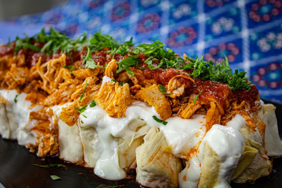 A 9x13 baking dish of baked chicken enchiladas covered in red sauce, melted cheese, sour cream, and fresh cilantro, photographed from above on a wooden surface