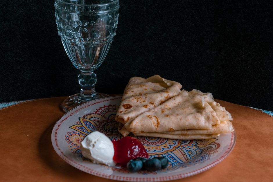 Stack of thin golden crepes on a white plate with fresh strawberries and a dusting of powdered sugar, photographed on a rustic wooden table