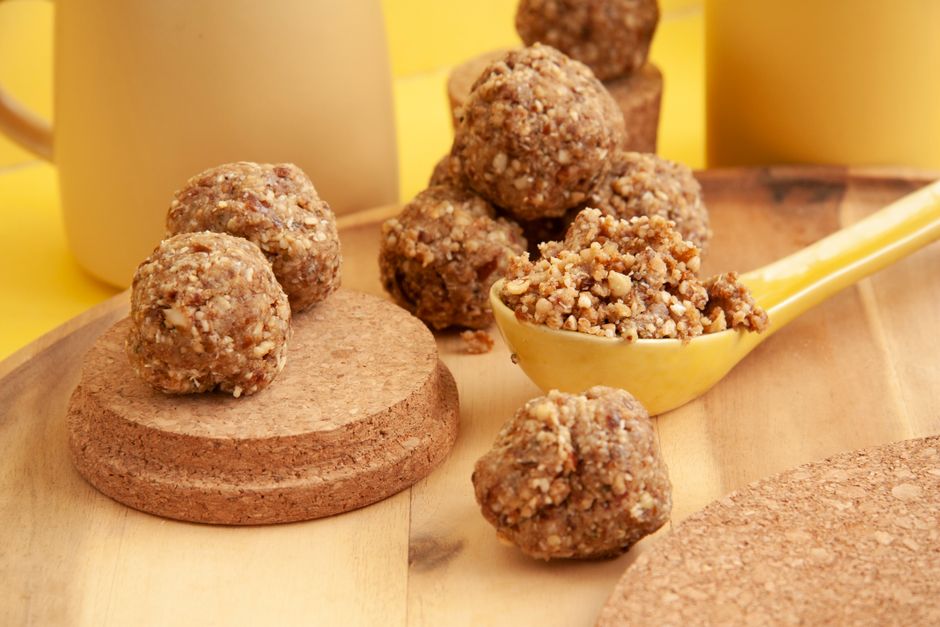 A wooden board holding two dozen round no-bake energy balls rolled in oats and studded with mini chocolate chips, with a jar of peanut butter and honey in the background