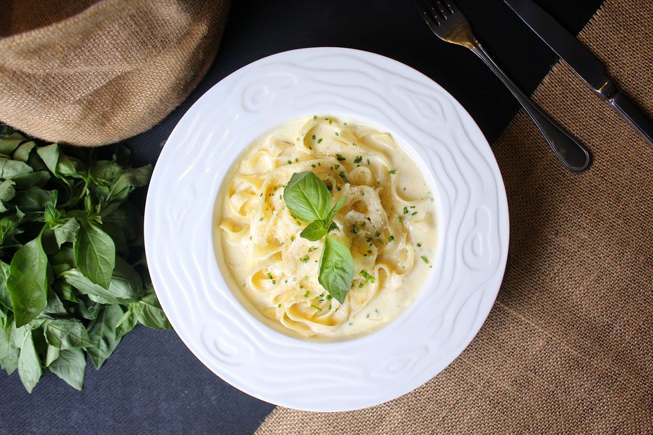 A bowl of fettuccine alfredo with silky cream sauce, freshly grated Parmesan, and cracked black pepper on a rustic wooden table
