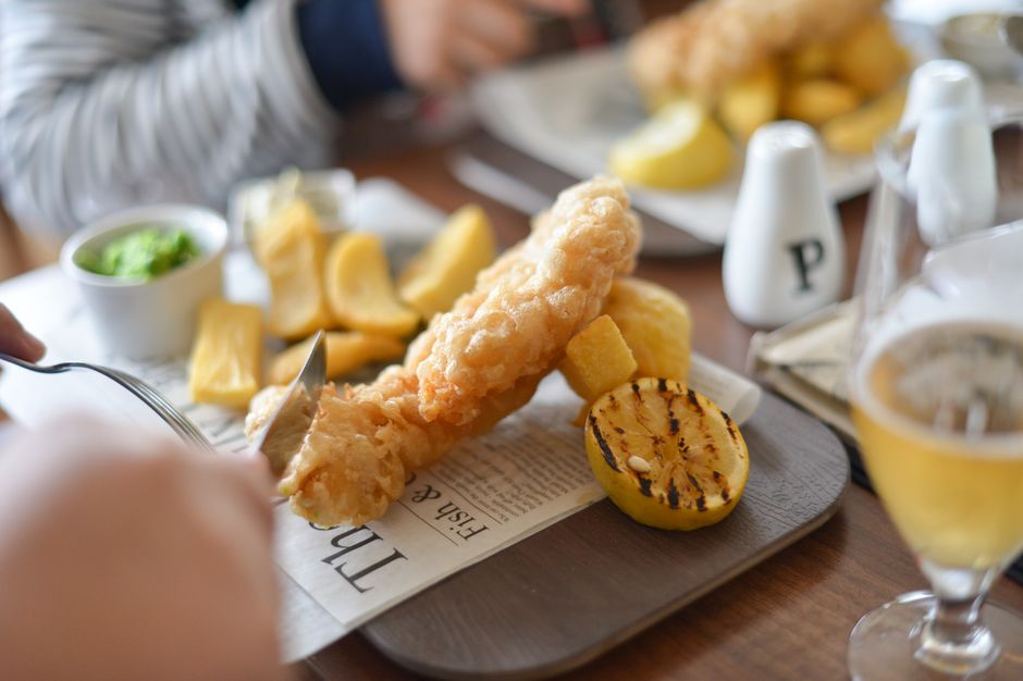 Golden beer-battered fish and chips served in a paper-lined basket with malt vinegar, lemon wedges, and tartar sauce on a rustic wooden table