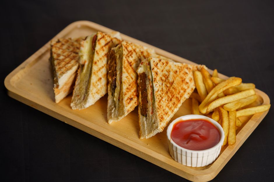 A french dip sandwich with thinly sliced roast beef and melted provolone on a toasted hoagie roll, served with a small ramekin of rich golden au jus for dipping on a wooden board