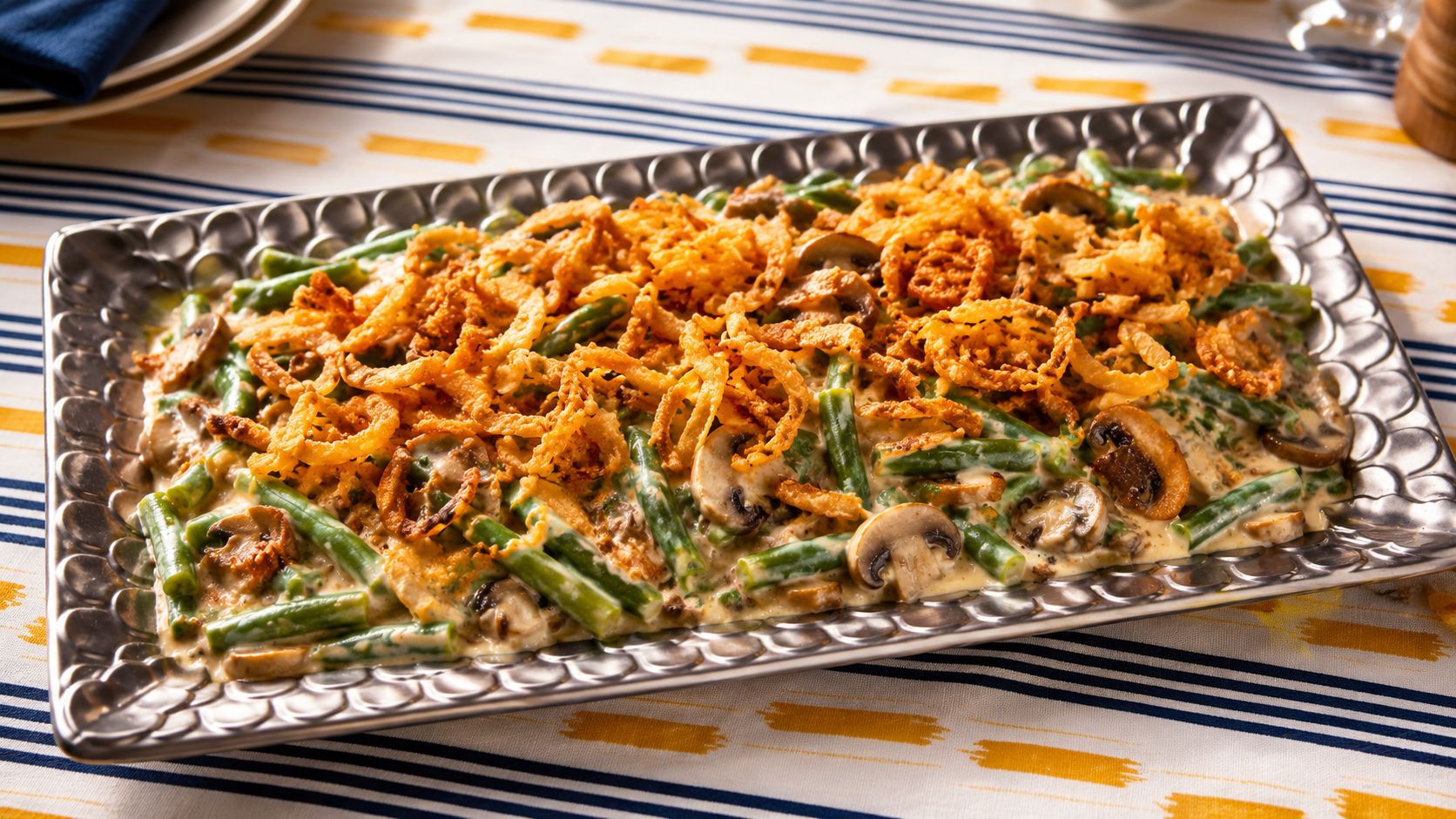 Bubbling green bean casserole in a white ceramic baking dish with a golden crispy fried onion topping, photographed from above on a wooden table