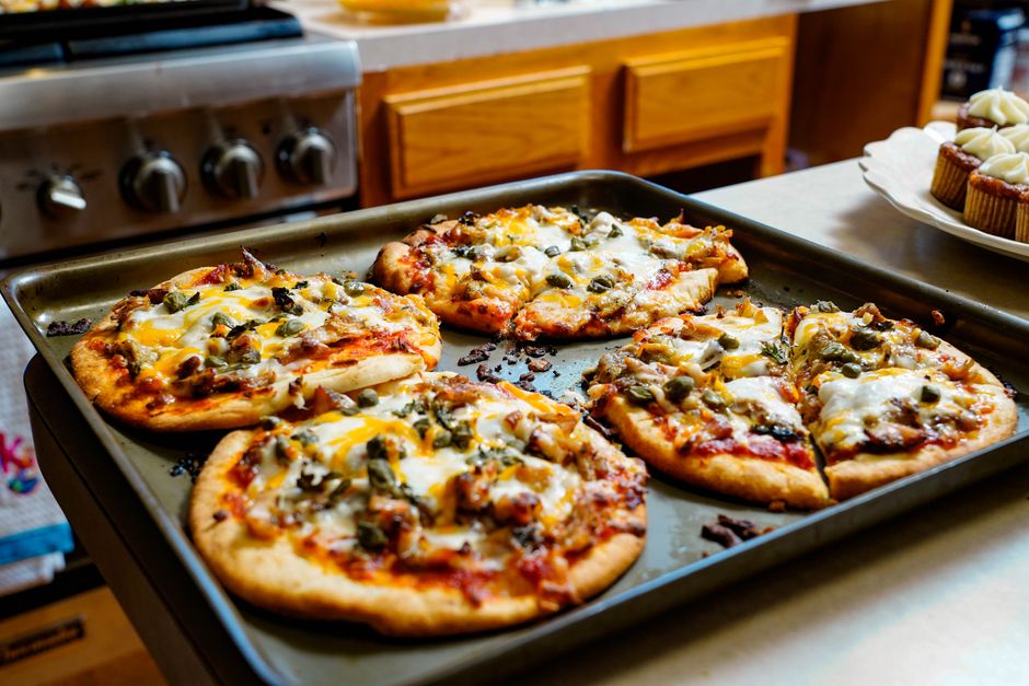 A homemade pizza on a wooden cutting board, crust golden and slightly charred at the edges, topped with melted mozzarella, pepperoni, and fresh basil leaves