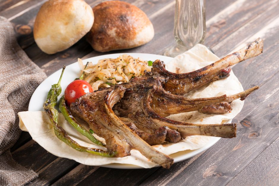 Pan seared garlic herb lamb chops on a white plate with golden crust, fresh rosemary sprigs, and a lemon wedge on the side
