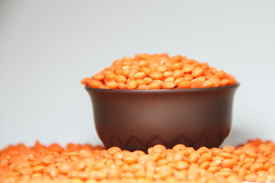 A bowl of homemade lentil soup with visible carrot and lentils, topped with fresh parsley, served with crusty bread on a wooden surface