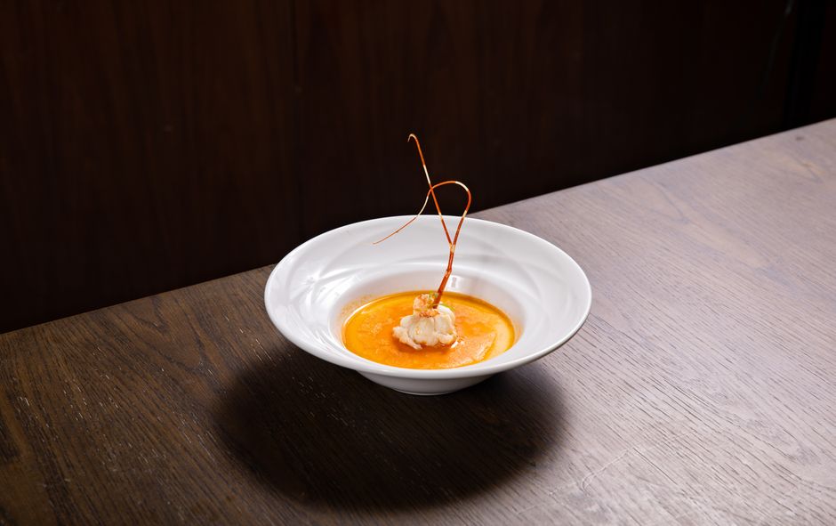 A bowl of homemade lobster bisque with a deep orange-red color, topped with fresh chives and a swirl of cream, served with crusty bread on a dark wooden surface