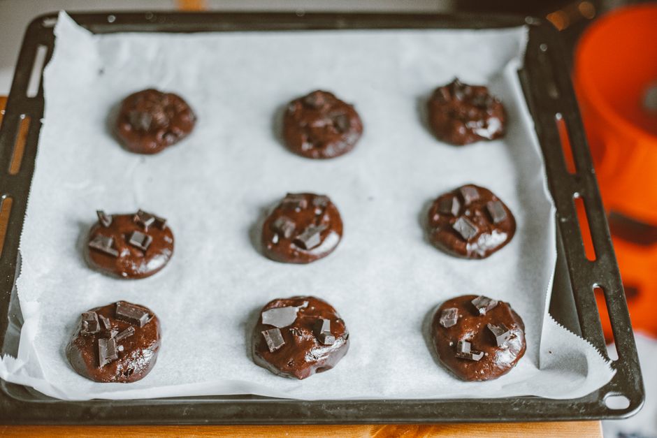 Overhead view of chocolate oatmeal no bake cookies set on wax paper, with a matte texture and glossy chocolate surface, arranged in rows on a wooden countertop