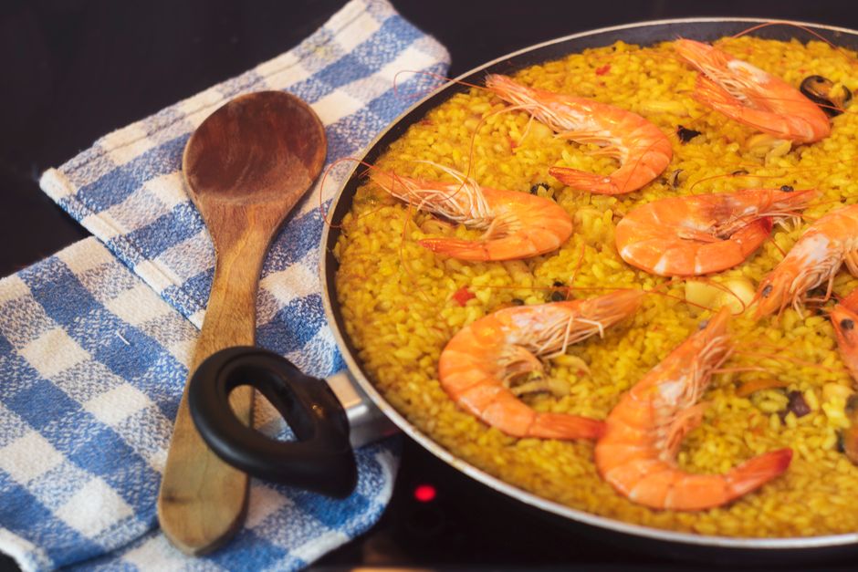 A golden seafood paella served in a wide pan, showing saffron-stained rice, pink shrimp, open mussels, and a crispy socarrat crust, garnished with parsley and lemon wedges