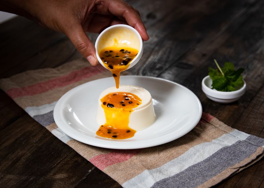 A plated classic vanilla panna cotta unmolded onto a white plate, topped with fresh strawberry coulis and halved strawberries, shot from slightly above on a marble surface
