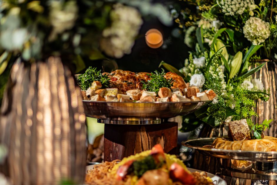 A white ceramic bowl of glossy honey-sriracha cocktail meatballs garnished with sliced green onions and sesame seeds, surrounded by toothpicks on a wooden party table