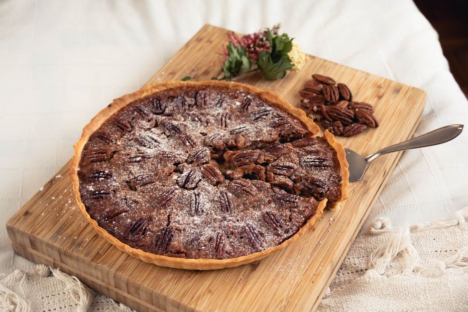 A whole pecan pie in a fluted pie dish with a golden-brown crust, topped with rows of toasted pecan halves in a rich dark caramel filling, cooled and ready to slice