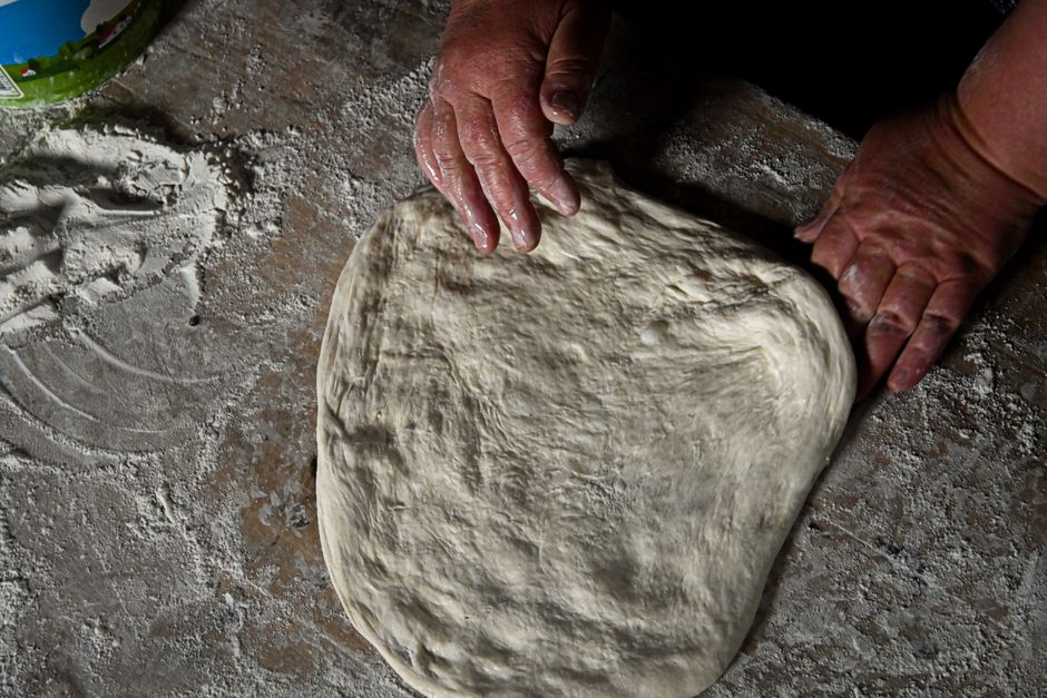 Freshly stretched homemade pizza dough on a floured wooden surface, slightly blistered and golden at the edges, ready for toppings