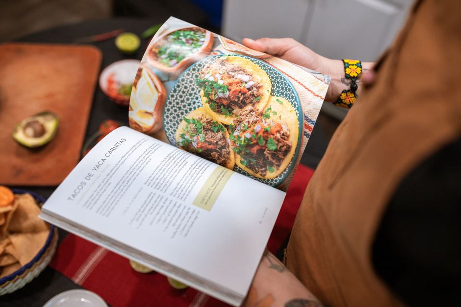A cast iron skillet of crispy pork carnitas with caramelized golden edges, garnished with lime wedges, white onion, and fresh cilantro, surrounded by warm corn tortillas