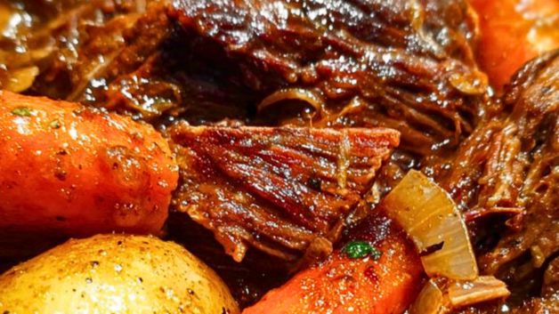 A Dutch oven filled with fall-apart pot roast surrounded by tender carrots and golden potatoes, bathed in rich brown gravy