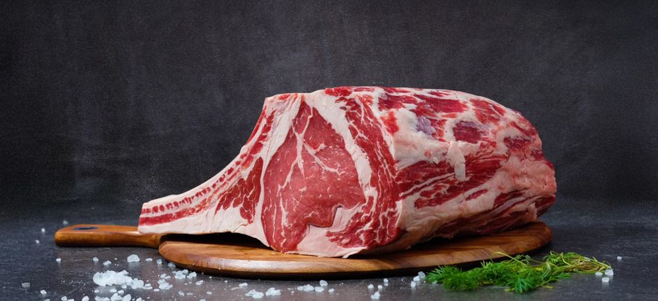 A sliced bone-in prime rib roast on a wooden carving board, showing a dark herb crust and a rosy pink medium-rare interior, garnished with fresh rosemary sprigs