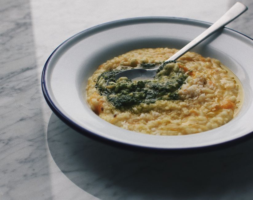 A wide bowl of creamy parmesan risotto garnished with freshly grated cheese and chopped parsley, served on a linen napkin with a wooden spoon