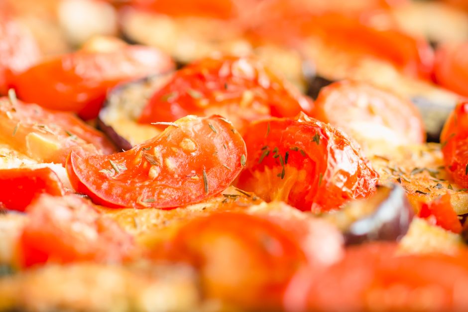 A sheet pan of golden roasted vegetables including zucchini, bell pepper, broccoli, and burst cherry tomatoes, topped with fresh parsley and a lemon wedge on the side