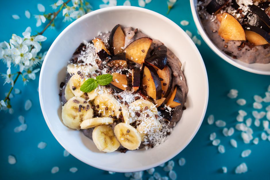 Overhead shot of a thick smoothie bowl with deep purple-pink base topped with rows of granola, sliced strawberries, fresh blueberries, chia seeds, and shredded coconut in a white ceramic bowl