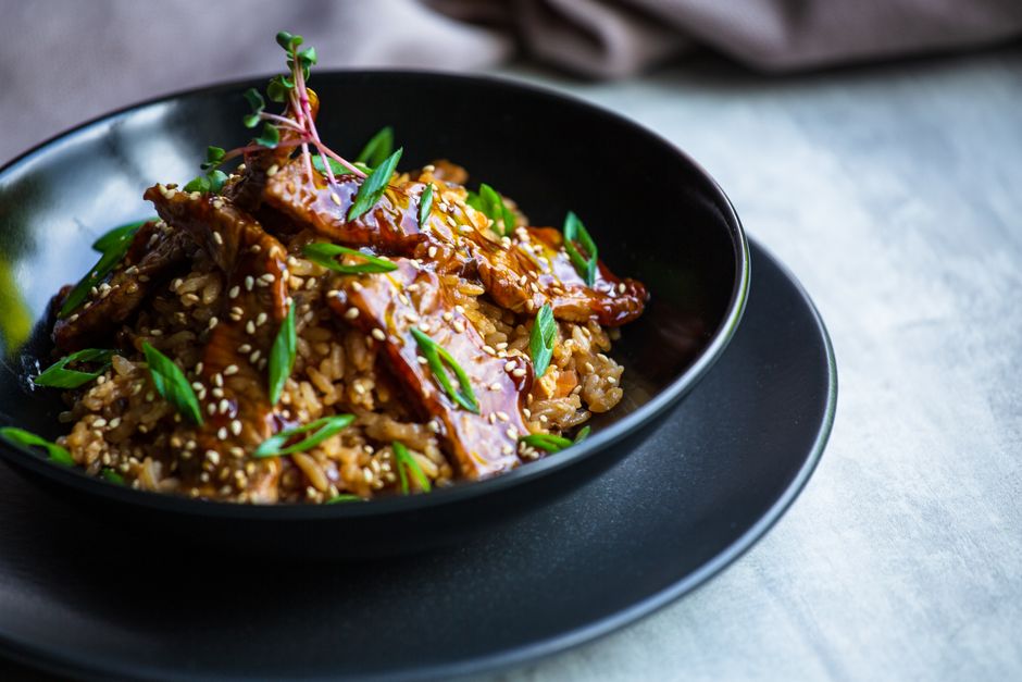 Homemade teriyaki sauce in a small glass jar with a spoon resting across the top, glossy and deep brown, with fresh ginger and garlic on a wooden cutting board nearby